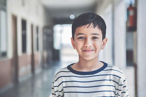 Close-up portrait of smiling 8-9 years Indian kid, standing straight at school campus in school uniform and looking at camera