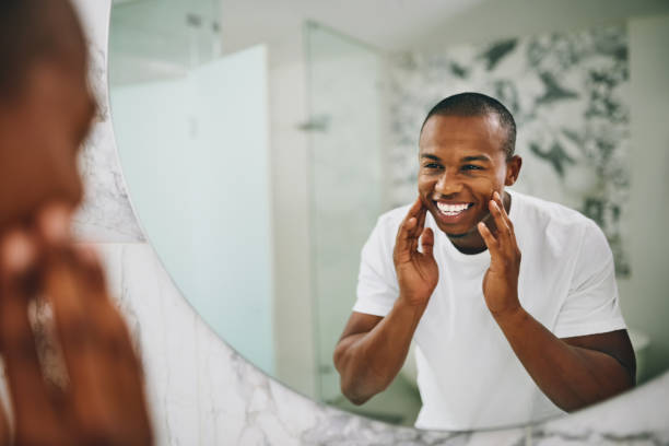 My skin just gets better and better Shot of a young man going through his morning routine in the bathroom at home looking in mirror stock pictures, royalty-free photos & images