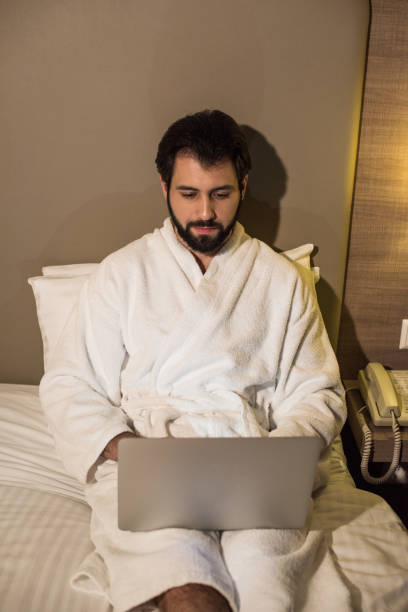 istock handsome man in bathrobe using laptop in bed at hotel suite in evening 941785668