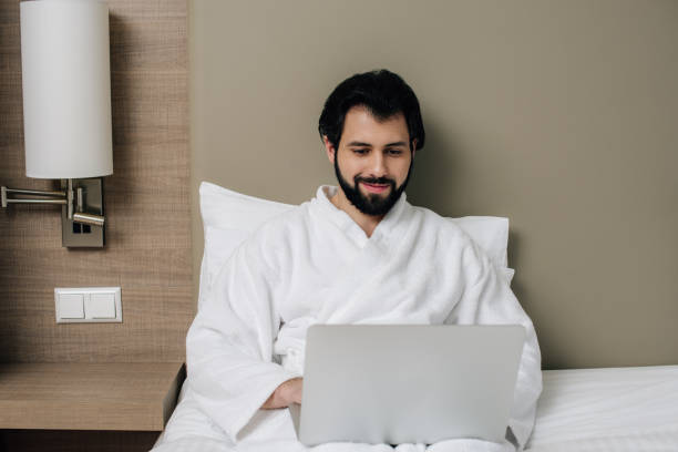 istock handsome man in bathrobe using laptop in bed at hotel suite 941785864