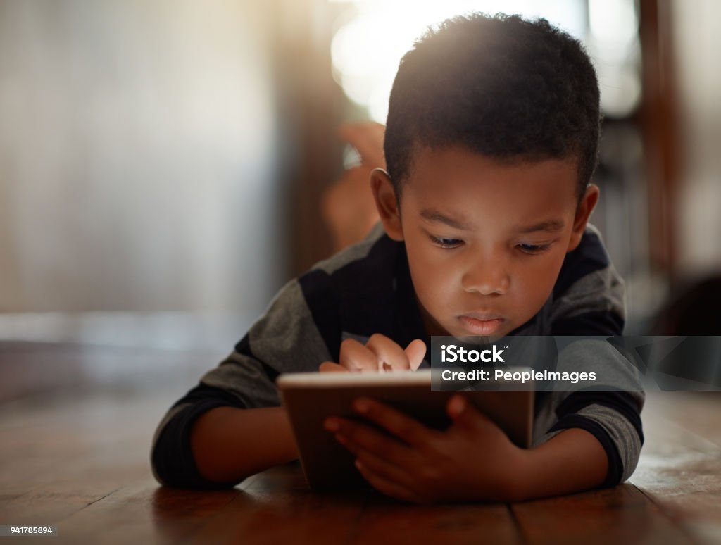 Growing up in a technology-based world Shot of a young boy using his digital tablet while lying on the floor at home Child Stock Photo