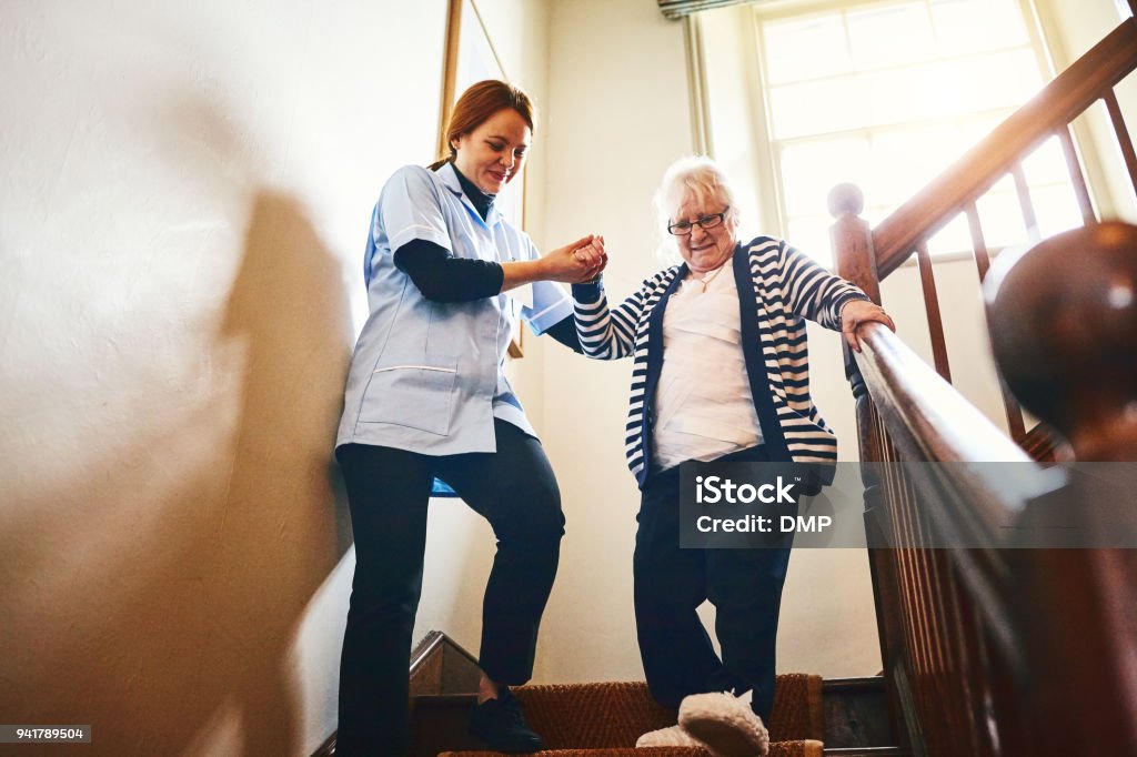 Caregiver helping senior woman walking down stairs Young female caregiver helping senior woman walking down stairs at home Senior Adult Stock Photo