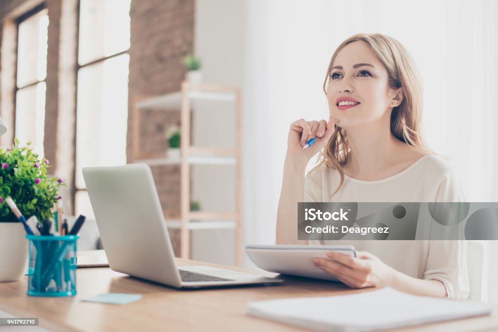 Portrait of young beautiful thoughtful lady sitting at the table working with laptop on writing down new ideas Women Stock Photo