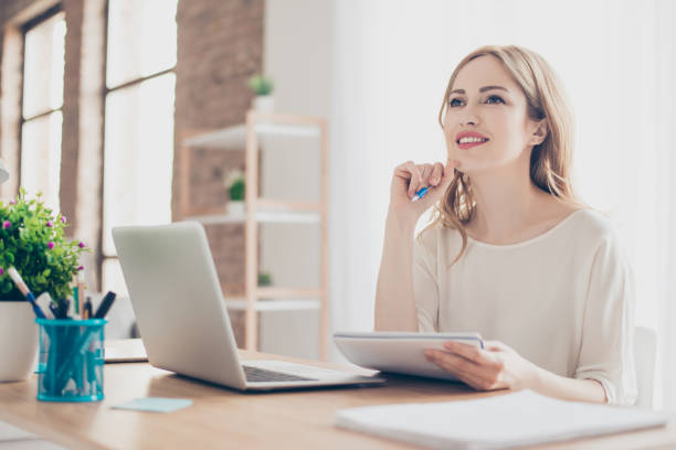 portrait of young beautiful thoughtful lady sitting at the table working with laptop on writing down new ideas - muse indoors lifestyles education imagens e fotografias de stock