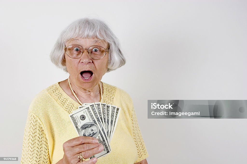 A surprised senior woman holding $100 bills Elederly woman holding a bunch of $100 bills with a surprised facial expression. Senior Women Stock Photo