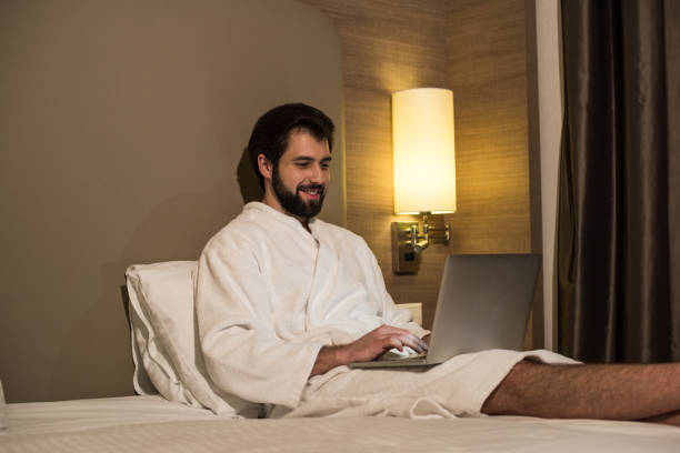 istock smiling man in bathrobe using laptop in bed at hotel suite in evening 941793744