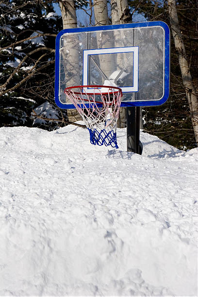 Sun shines brightly on the winter day with snow splattered on the basketball hool.
