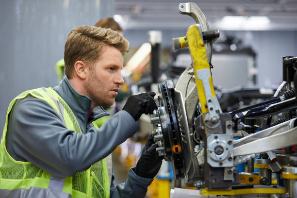 Confident male engineer examining car chassis Confident mid adult engineer examining car chassis at automobile industry. Handsome male supervisor is working on car part in factory. He is wearing reflective clothing. automobile industry stock pictures, royalty-free photos & images