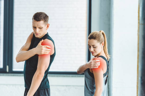 pareja joven teniendo dolor en los brazos después de hacer ejercicio en el gimnasio - stretching boyfriend indoors lifestyles fotografías e imágenes de stock