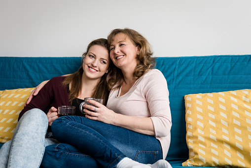 Mother with her loving daughter sitting on sofa in apartment