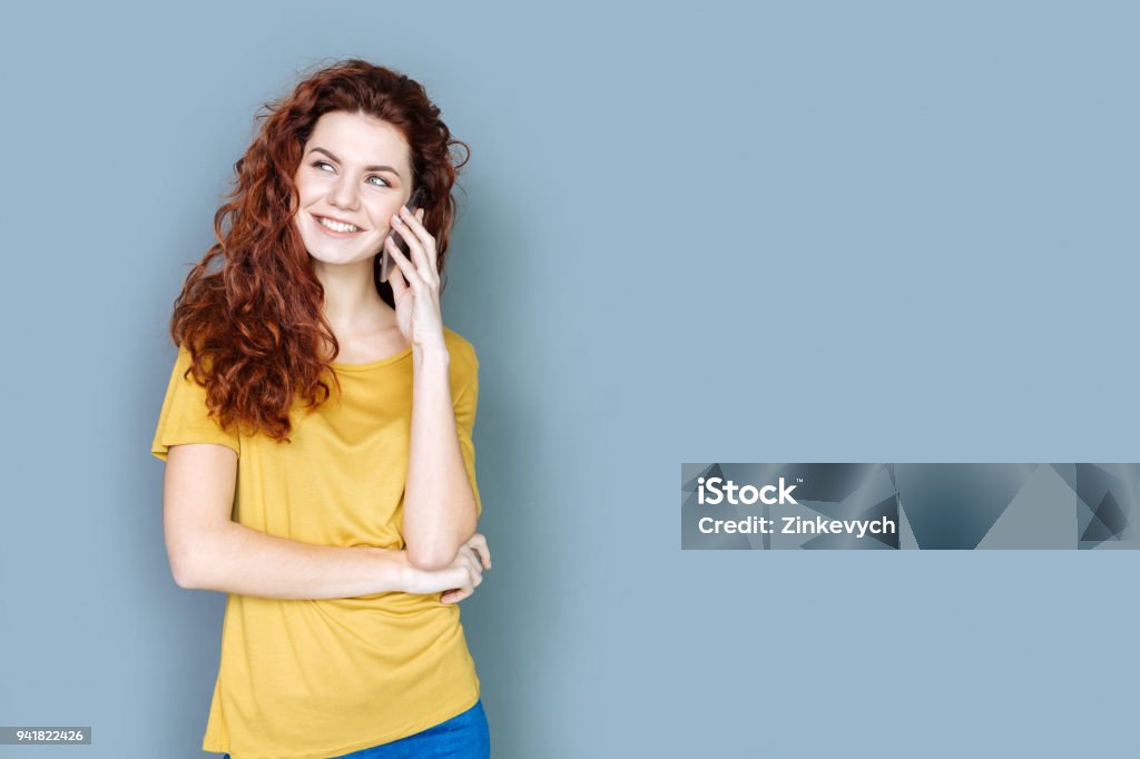 Joyful attractive woman having a phone conversation Pleasant communication. Joyful attractive young woman smiling and having a phone conversation while standing against blue background Adult Stock Photo