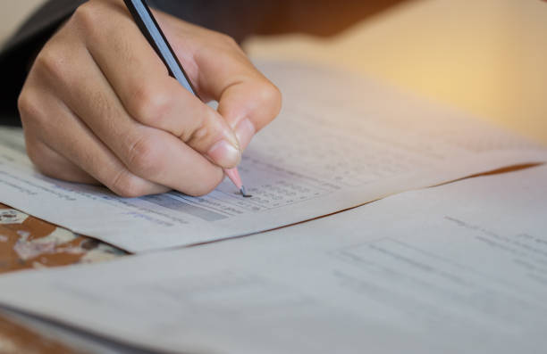 istock Front view Asian Students, undergraduate holding pencil writing on multiple-choice quizzespaper answer sheet and sitting on old lecture chair in final exam classroom, Education  literacy concept. 941826502