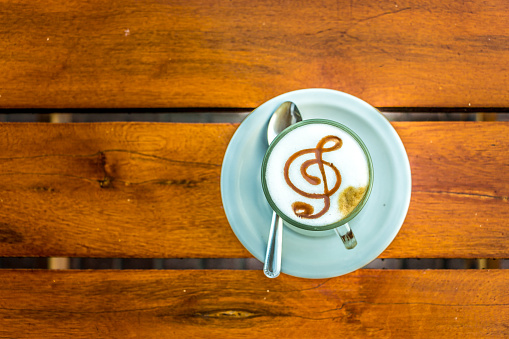 Top view of a hot coffee cappuccino with the treble clef G on the top of the foam, wooden background.