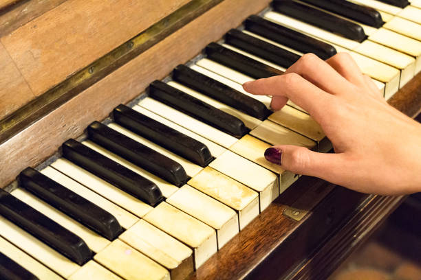 A hand of a female young woman with colored nails playing a very old piano with ivory keys.