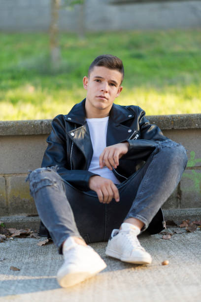 istock Stylish young man in leather jacket looking at camera, sitting in a park 941841464