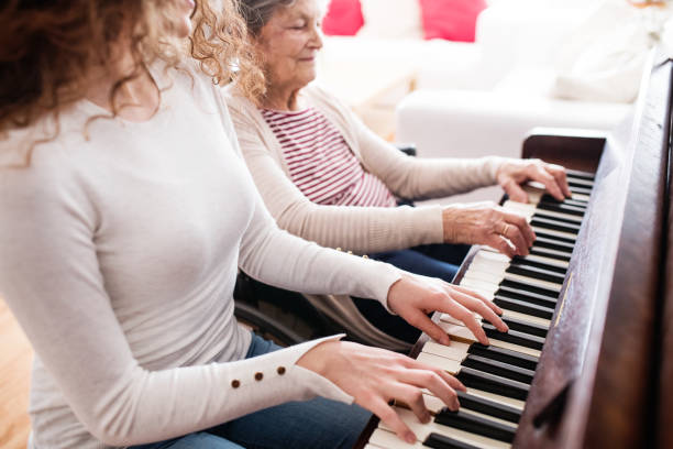 A girl with grandmother in wheelchair playing the piano. A teenage girl with grandmother in wheelchair playing the piano at home. Family and generations concept. roots music stock pictures, royalty-free photos & images