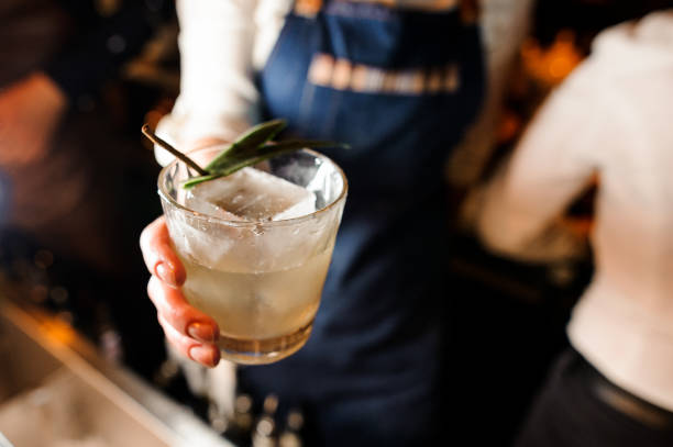 Waitress dressed in a white shirt and blue apron holding a glass with cold drink Waitress dressed in a white shirt and blue apron holding a glass filled with cold alcoholic drink with ice cubes tequila drink stock pictures, royalty-free photos & images
