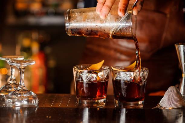 Bartender pouring alcoholic drink into the glasses Bartender pouring fresh alcoholic drink into the glasses with ice cubes on the bar counter vodka photos stock pictures, royalty-free photos & images