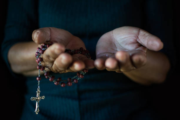 istock Close up of old hands praying on black background 941886322