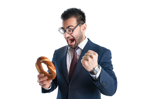 Geeky, wacky and eccentric looking man in blue suit and funny glasses fist pumping in excitement, looking at a Turkish bagel or simit
