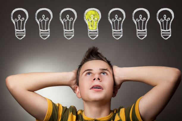 istock Young boy looking up at light bulb above head 941906026