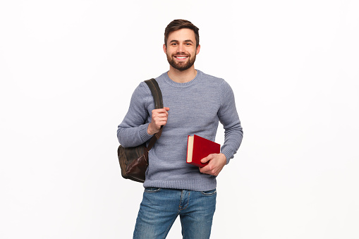 Content young man in casual outfit posing with backpack and textbook isolated on white.