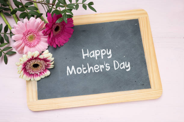 istock three gerbera flowers on a writing chalkboard, text Happy Mother's Day, bright pink background, top view from above 941912748