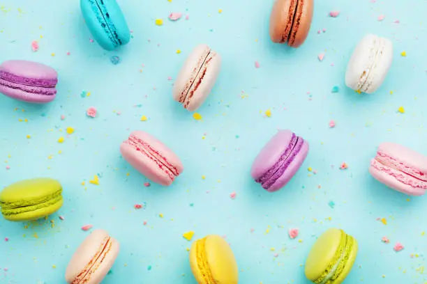 Colorful cake macaron or macaroon on turquoise pastel background from above. French almond cookies on dessert top view. Punchy pastel.