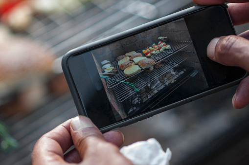 Asian Man photographs afood on a barbecue grill with his smartphone