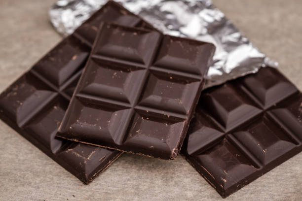 barrette di cioccolato fondente su foglio e carta gialla - cioccolato fondente foto e immagini stock