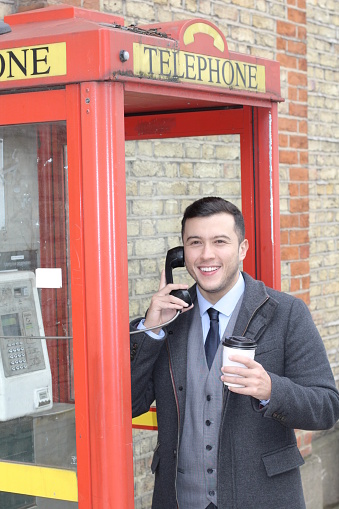 Stylish ethnic gentleman calling from vintage payphone.