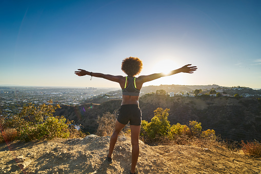 athletic african american woman celebrating reaching top of runyon canyon with arms open shot with lens flare