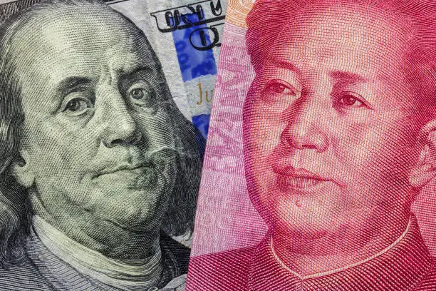 Close up of one hundred Dollar and 100 Yaun banknotes with focus on portraits of Benjamin Franklin and Mao Tse-tung/USA vs China trade war concept