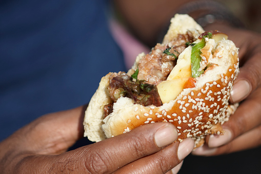Close up of a Halal lamb burger with cheese and salad in a seeded bun held by an Asian Male