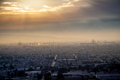 Cityscape of Long Beach and the Andeavor Refinery in Carson from Hilltop Park in Signal Hill, with the Palos Verdes hills in the background at sunset on a hazy and cloudy day.