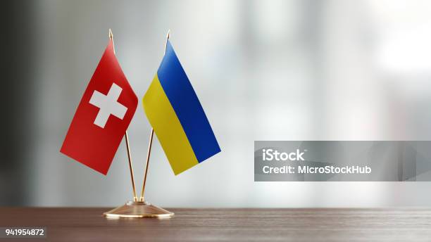 Swiss And Ukrainian Flag Pair On A Desk Over Defocused Background Stock Photo - Download Image Now