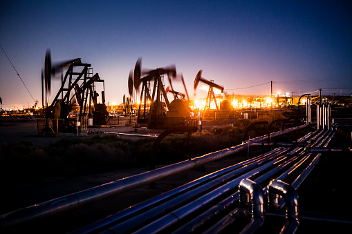 Oil pumpjacks pumping with long exposure motion blur at night as lights glow across the maze of above ground pipelines, Midway-Sunset Oil Field, Kern County, California.