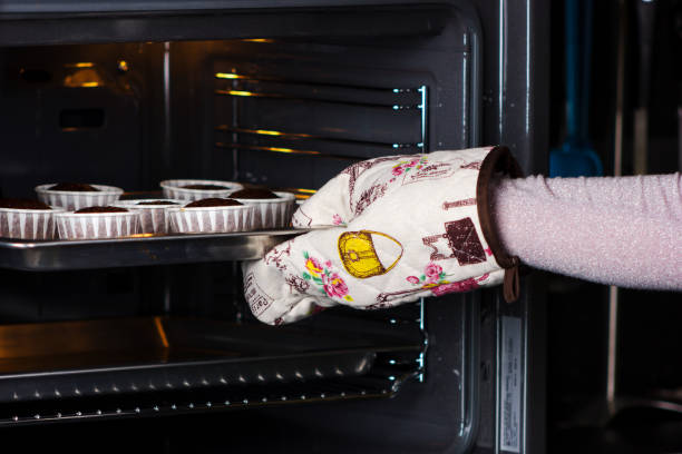 Woman`s hand in culinary mitten  getting chocolate cupcakes from oven in kitchen