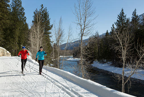 A man and woman cross country skiing on a groomed trail.