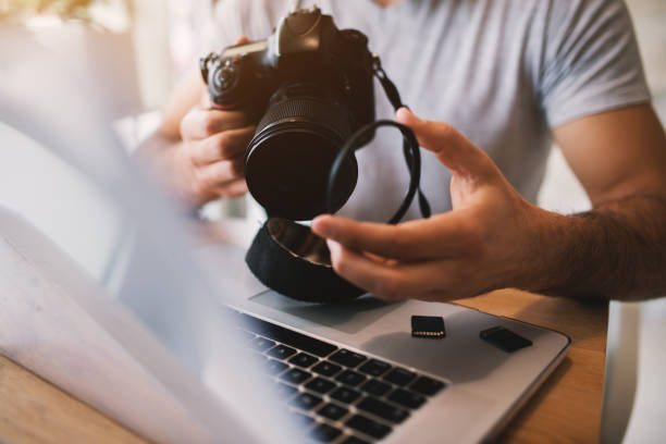 istock Man taking off lens of a professional camera while using a laptop. 941994306