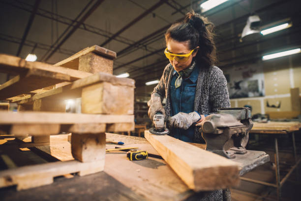 istock Portrait view of hardworking middle aged professional female carpenter worker working with sandpaper and choosing wood in the workshop. 942001604