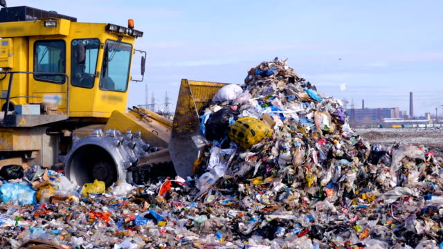 A high pile of trash moved by a landfill truck. Water, air contamination concept.