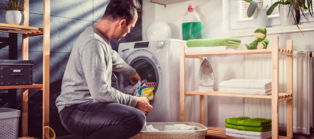 istock Man putting clothes into washing machine 942114550