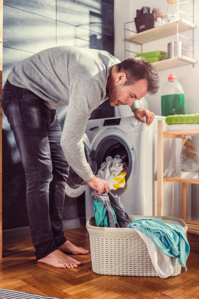 istock Man putting clothes into washing machine 942115126