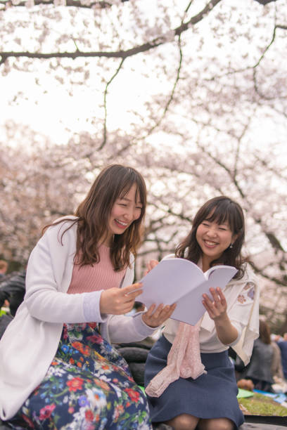 istock Happy female friends reading book under cherry blossom 942119504