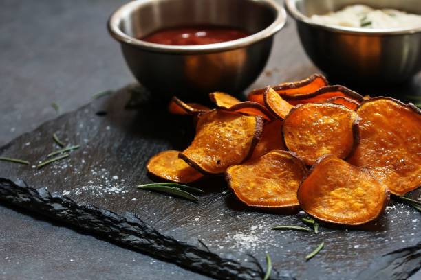 istock Homemade baked sweet potato chips with dips on dark moody background, selective focus 942121580