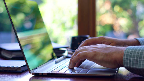 istock Man using touch screen laptop at desk in front of window, close up 942123408