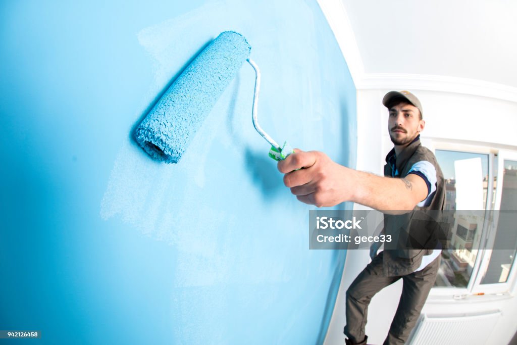 Young man painting a wall blue with a roller Painting - Activity Stock Photo