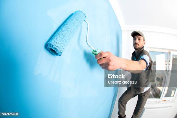 Young Man Painting A Wall Blue With A Roller Stock Photo - Download Image Now - Painting - Activity, Building Contractor, House Painter