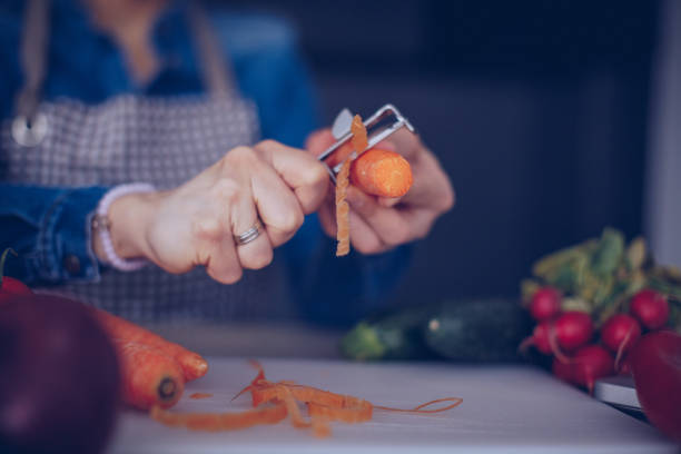 One woman, homemaker making a vegetarian lunch in kitchen alone, peeling a carrot , part of.